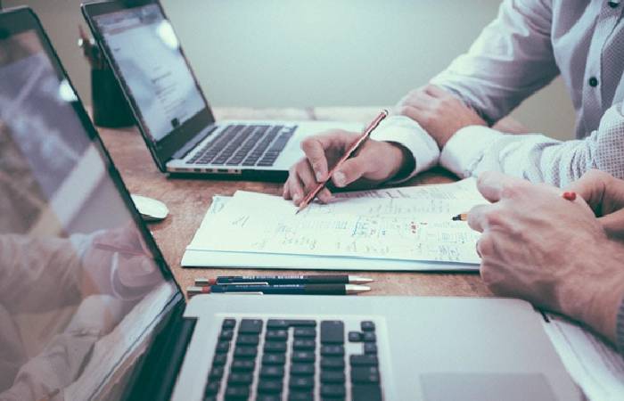 Two employees go over reported data together at a conference table.